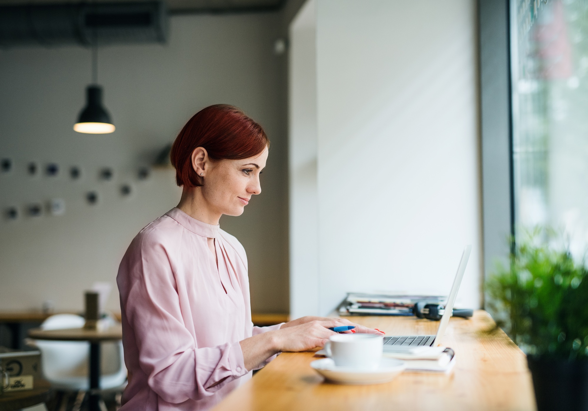 A portrait of woman with coffee sitting at the table in a cafe, using laptop