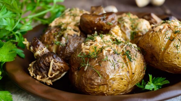 Baked potatoes with mushrooms, cheese and herbs on dark wooden background. Close up.