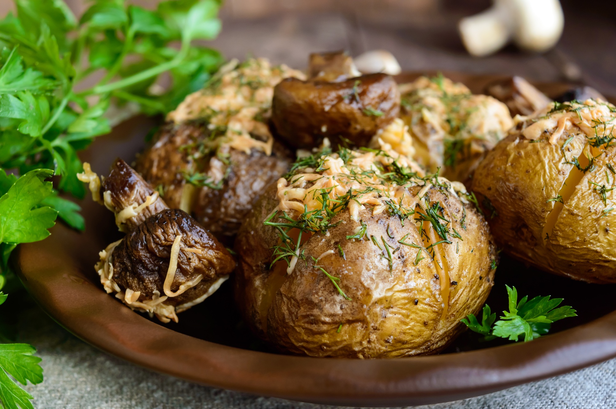 Baked potatoes with mushrooms, cheese and herbs on dark wooden background. Close up.
