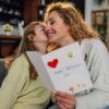 Daughter kissing mother and giving her a handmade greeting card for mother's day