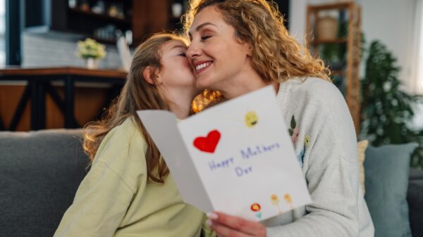 Daughter kissing mother and giving her a handmade greeting card for mother's day