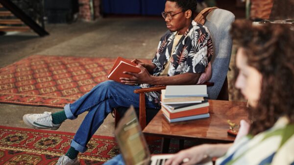Serious guy opening book in brown cover while sitting in armchair in living room